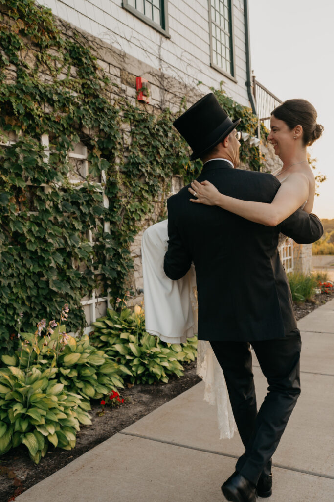 Groom embraces bride in front of the ivy-covered wall as they walk the garden path