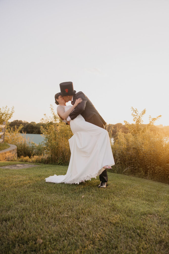 Groom dips bride back for a kiss in a golden field at sunset