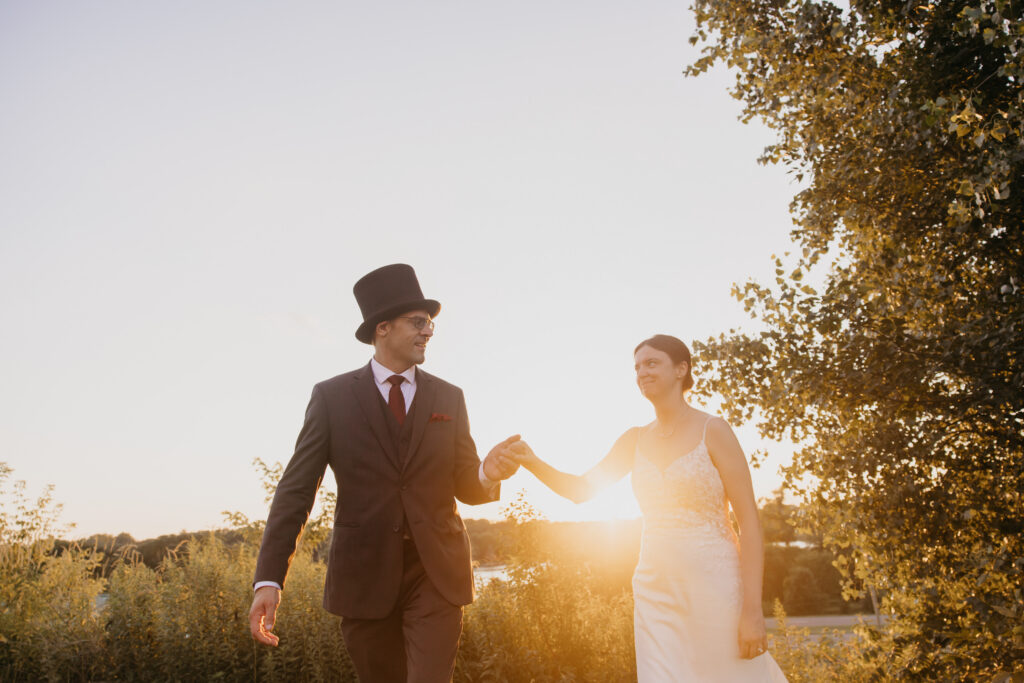 Bride and groom walk together through the field, silhouetted against the setting sun