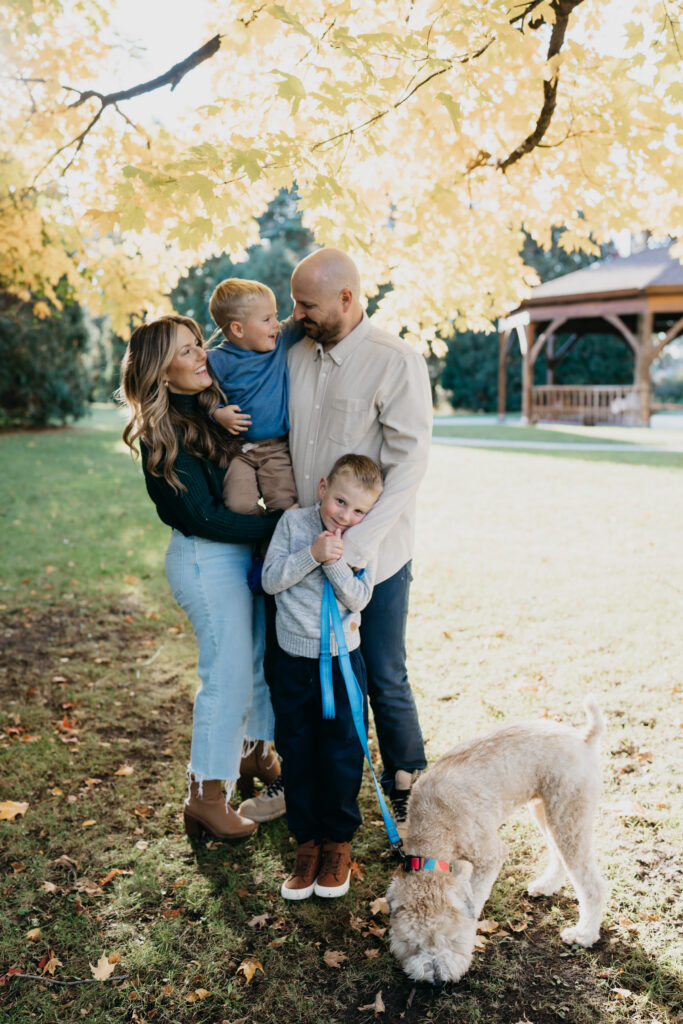 Family of four standing together with their dog on a leash, gazebo visible behind them
