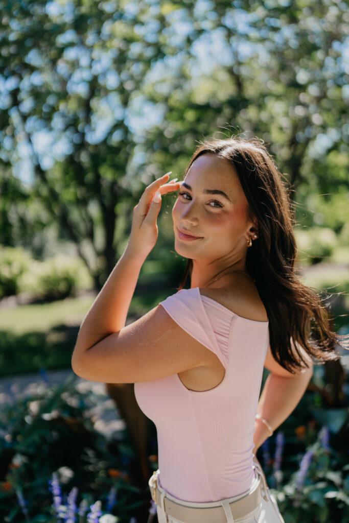 Senior girl in a pink cutout top posing among purple wildflowers in a garden