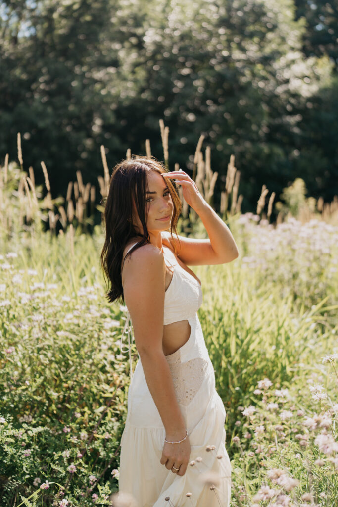 Senior girl in a cutout white dress standing in a field of wildflowers