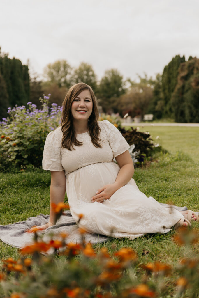 Pregnant woman sitting on a blanket in a wildflower field, one hand on her belly