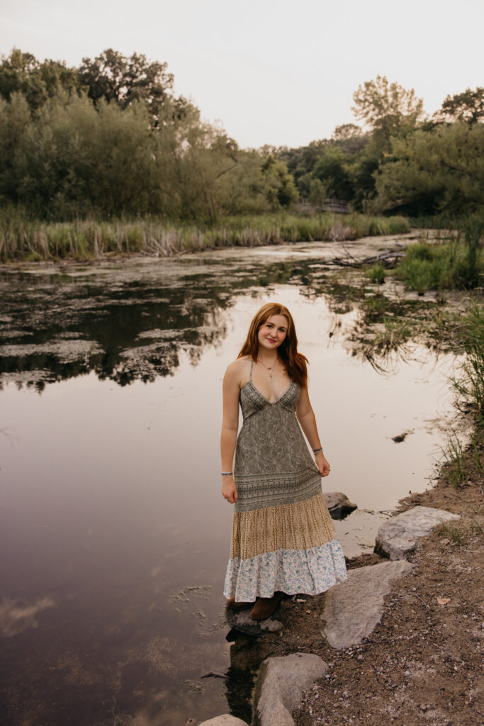 Senior standing on rocks at the water's edge, full-length portrait