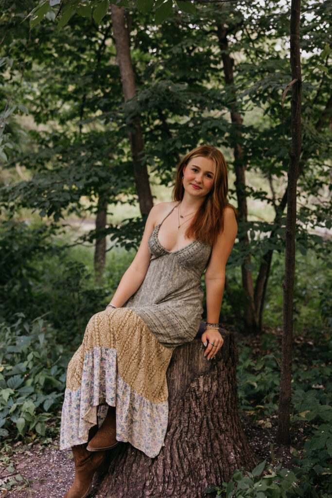 Senior sitting on a tree stump in a sage dress with a tiered lace hem