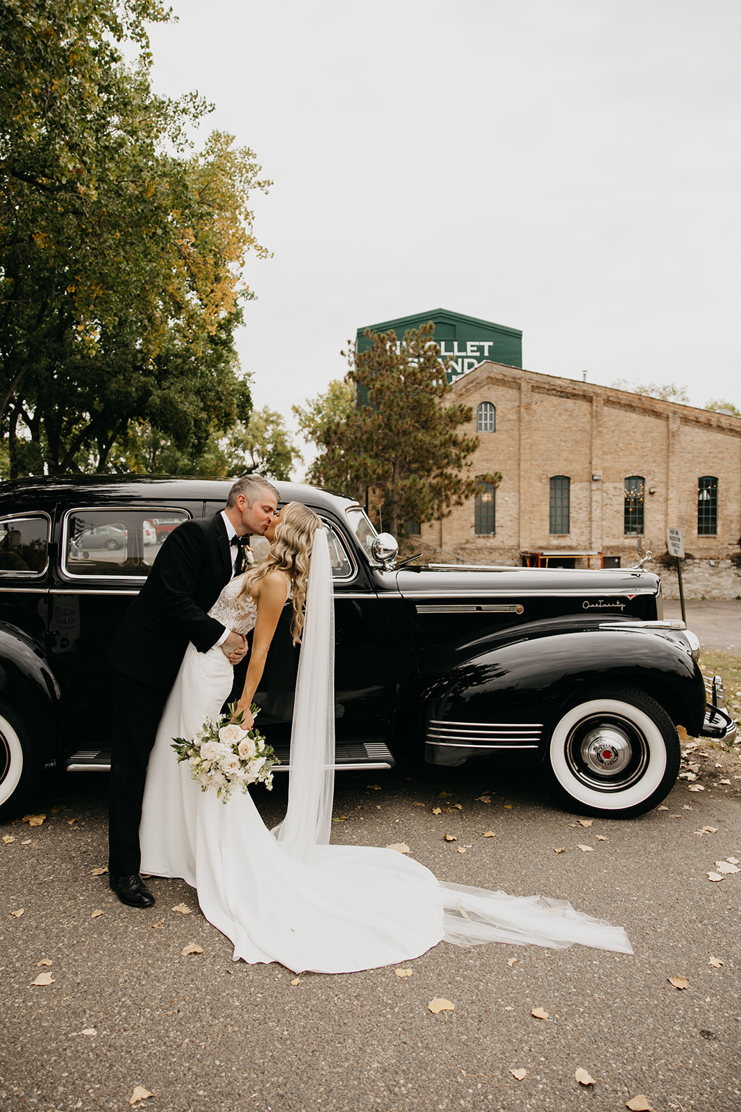 Bride and groom kissing beside a vintage black car outside Nicollet Island Inn in Minneapolis
