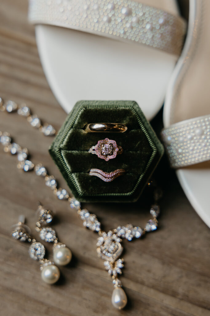 Bridal jewelry and rings displayed in a green velvet box beside white heels