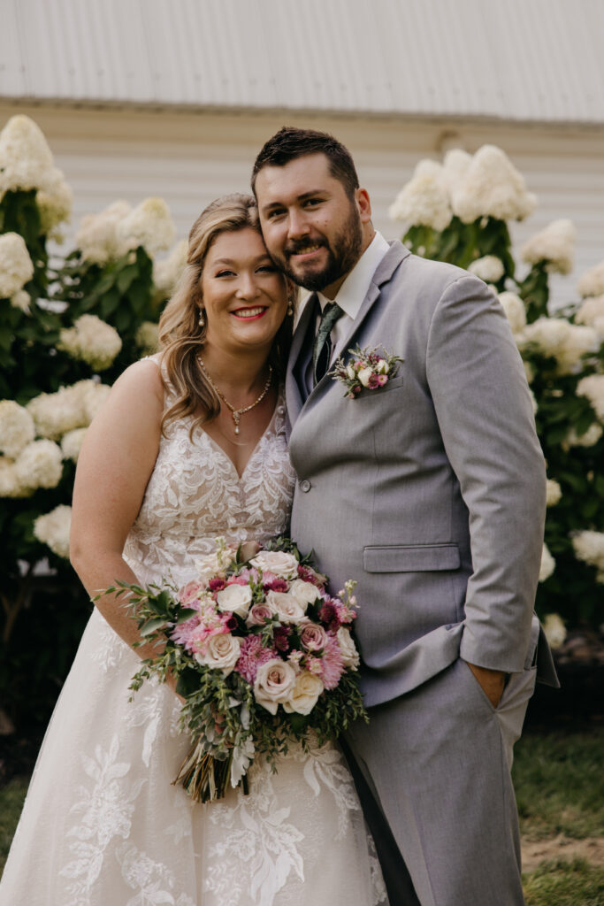 Bride and groom smile close together, groom's arm around her shoulders