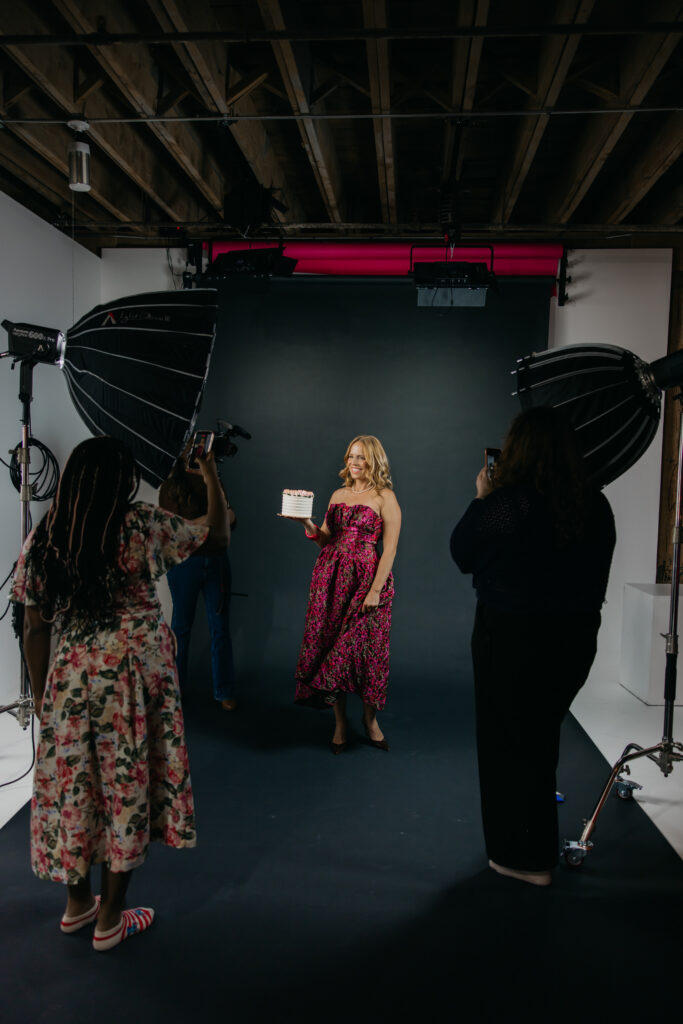 Creative business owner holding the skirt of a pink floral gown while a photography team captures the shot