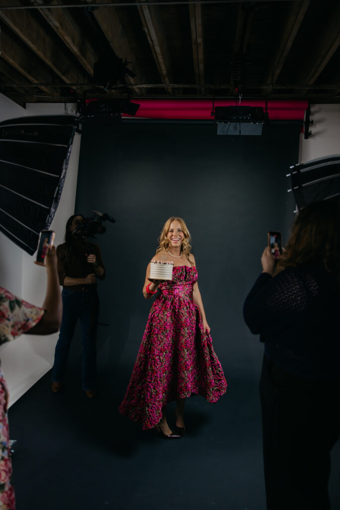 Creative business owner posing in a pink floral gown as a team photographs and films the session