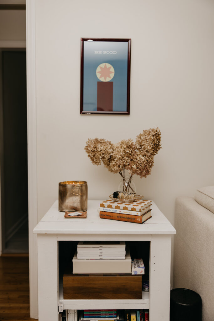 Styled entryway table with framed art, dried florals, and books beside a cream sofa