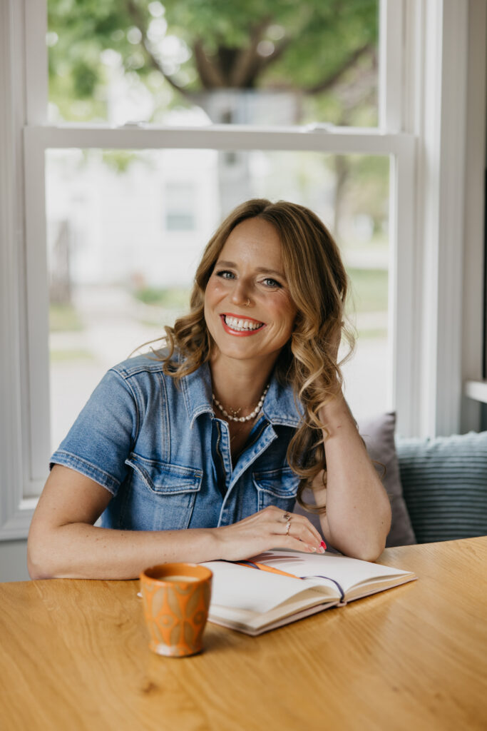 Creative business owner smiling at a wooden table with an open journal and coffee mug