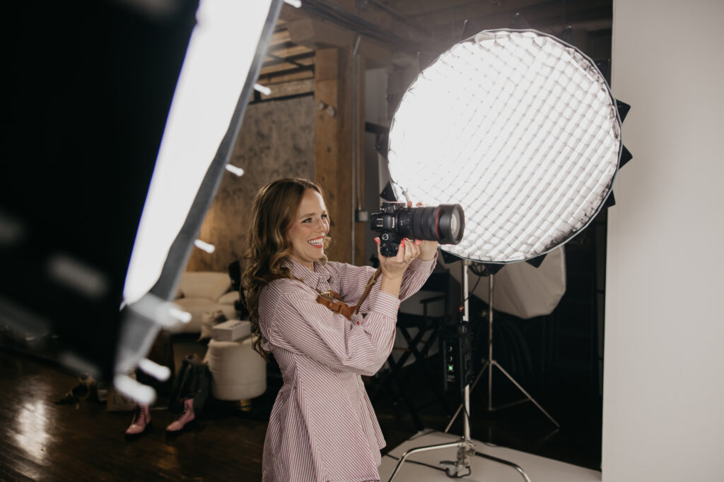 Photographer in a striped shirt smiling while shooting beside a large softbox in a Minneapolis studio