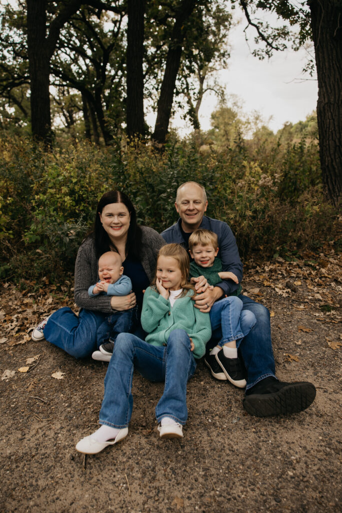 Family of five sitting together outdoors, dad holding baby while two older kids lean in