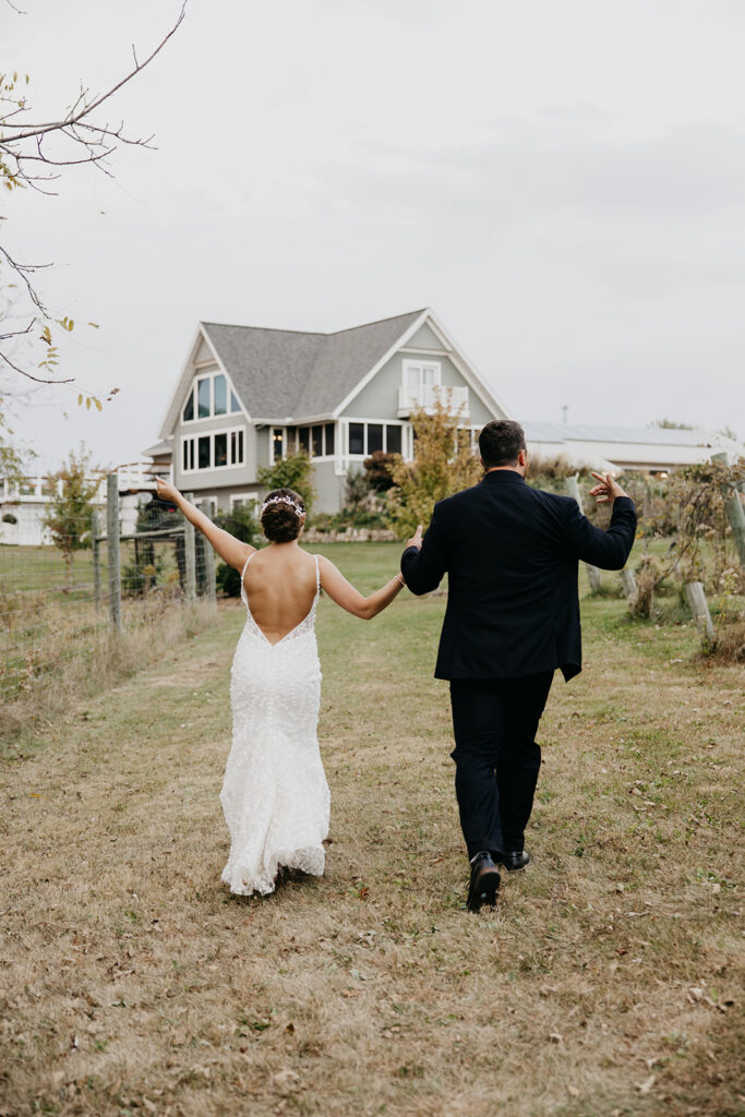 Bride and groom holding hands walking toward a farmhouse wedding venue