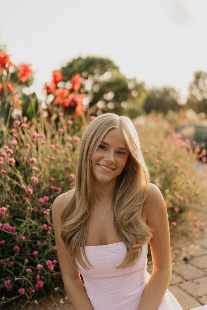 Senior smiling among pink and orange garden flowers during golden hour