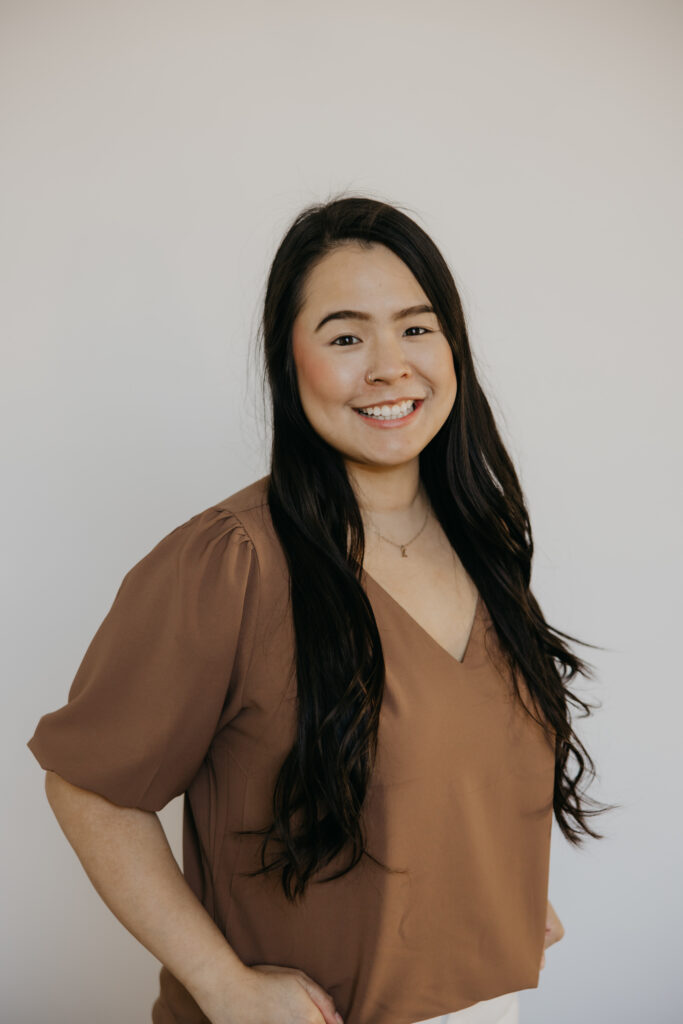Woman with long dark hair in a brown V-neck blouse smiling during her headshot session