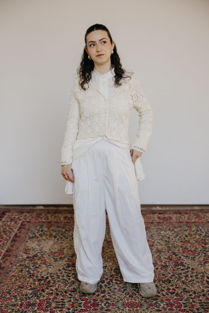 Woman in a white lace cardigan and wide-leg white trousers standing on a vintage rug