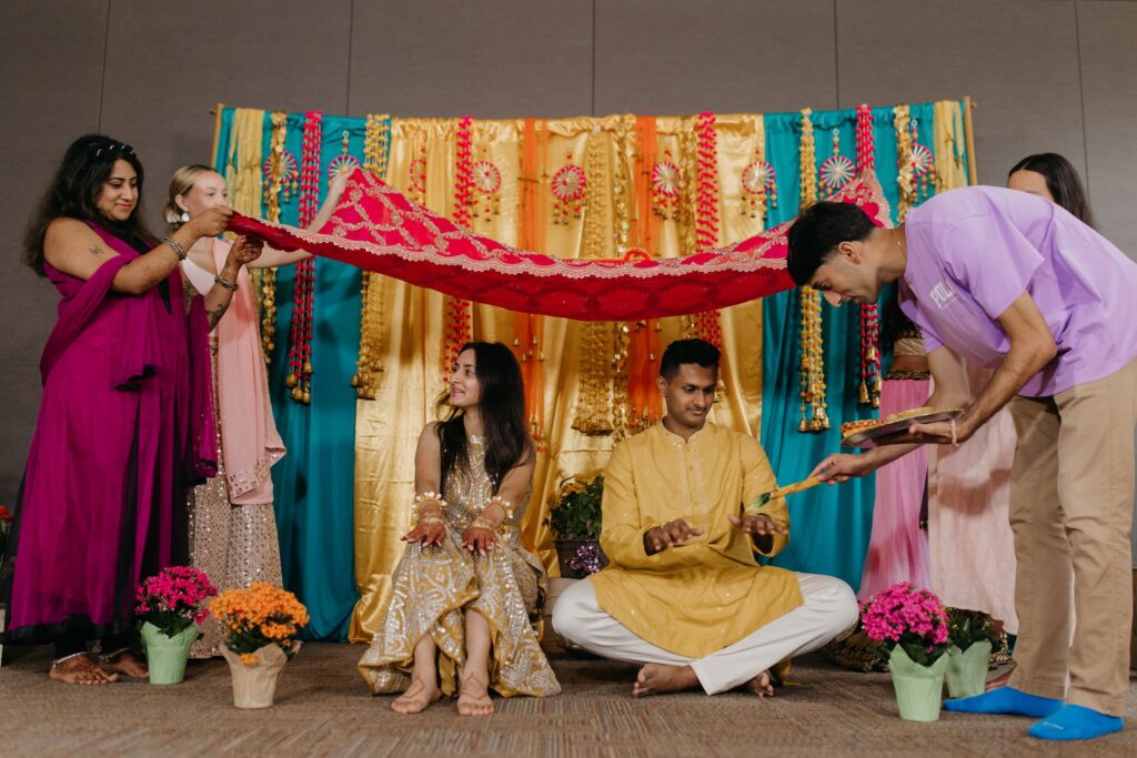 Family holding a red canopy over the couple during a haldi ceremony at their multi-day wedding