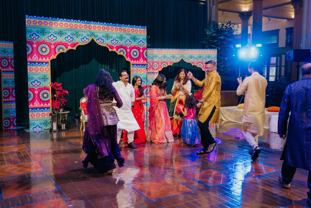 Family dancing in front of a vibrant patterned backdrop during a sangeet night celebration