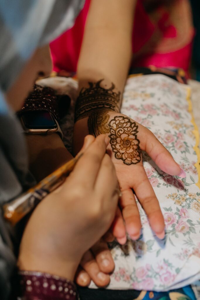 Close-up of a henna cone tracing a detailed mehndi design across the back of a hand