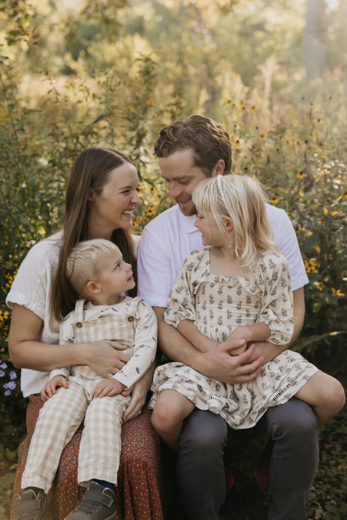 Mom and dad laughing face to face with toddler son and older daughter seated between them