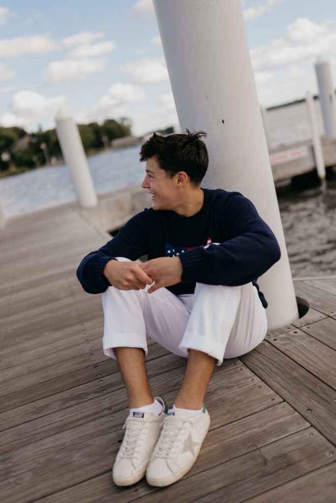 Senior guy in an American flag sweater sitting on a lakeside dock beside white posts