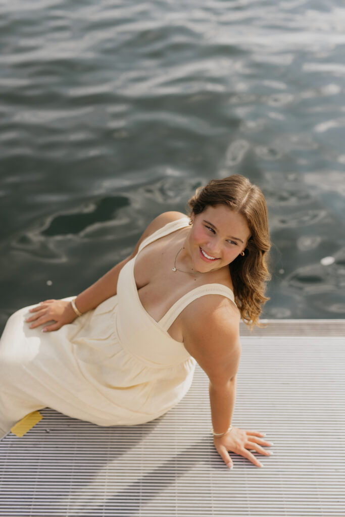 Senior girl posing on the dock looking down at the water in a cream dress