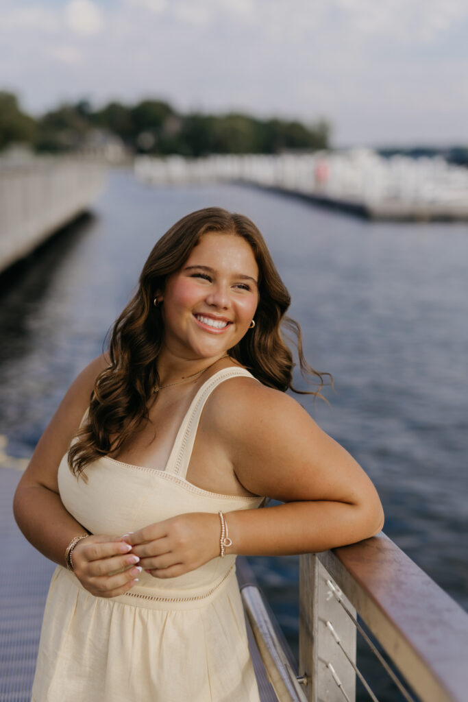 Senior girl leaning on a dock railing smiling in a cream dress