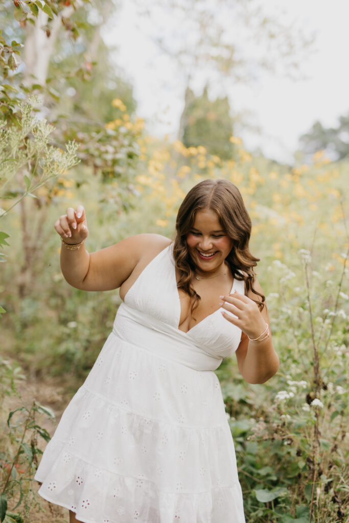 Joyful senior in a white eyelet dress laughing among yellow wildflowers and trees