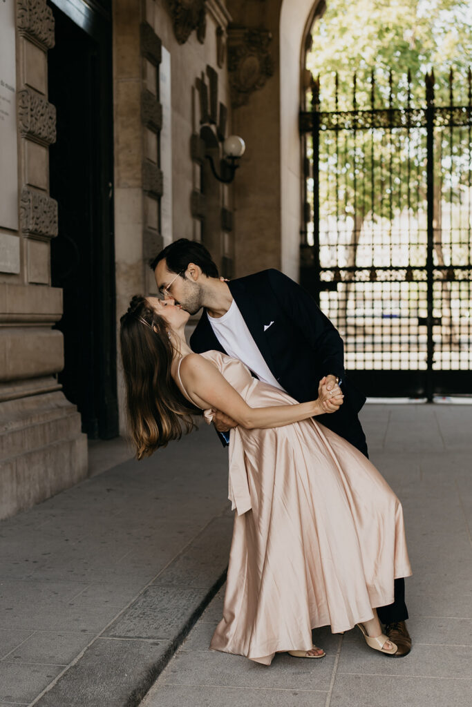 Engaged couple sharing a dipped kiss under an archway gate in Paris