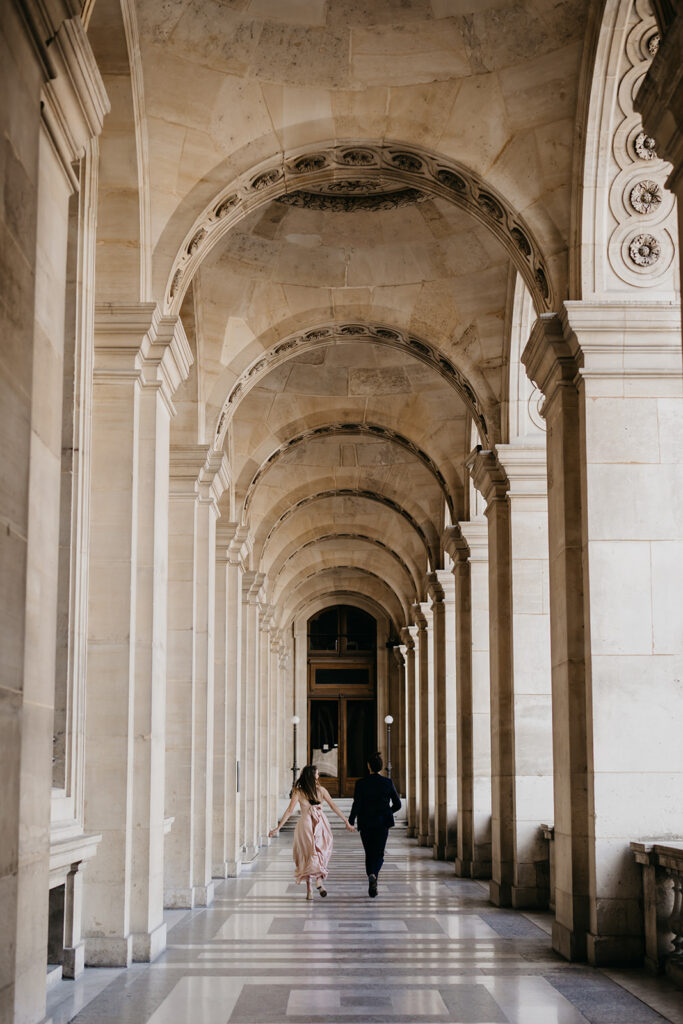 Engaged couple walking away together under a Paris colonnade