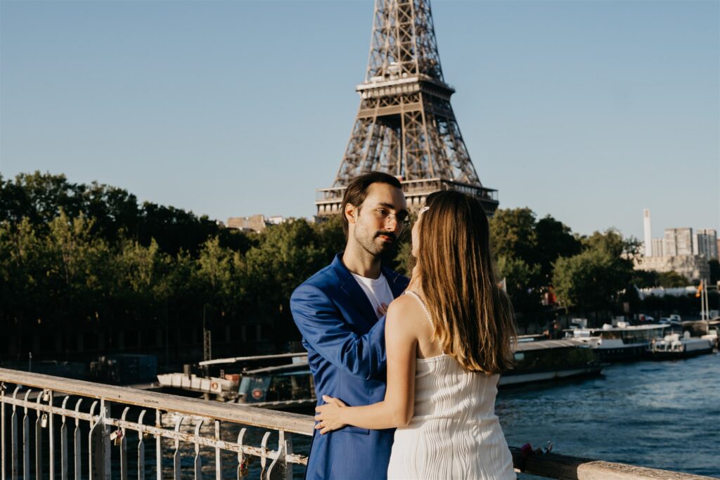 Engaged couple embracing on a Paris bridge with the Eiffel Tower in the background