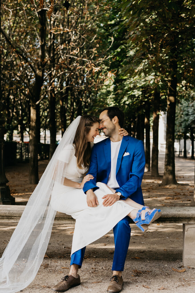 Engaged couple embracing on a bench under tree cover near the Louvre in Paris