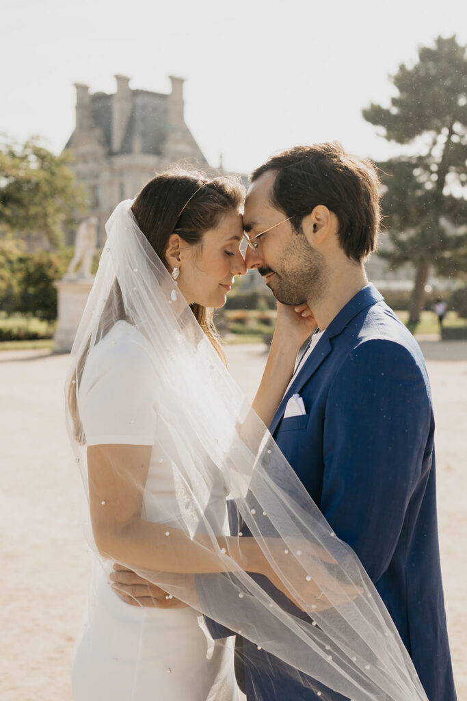 Engaged couple standing forehead to forehead under a veil at the Louvre in Paris