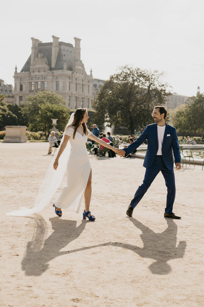 Engaged couple walking hand in hand across the Louvre courtyard in Paris
