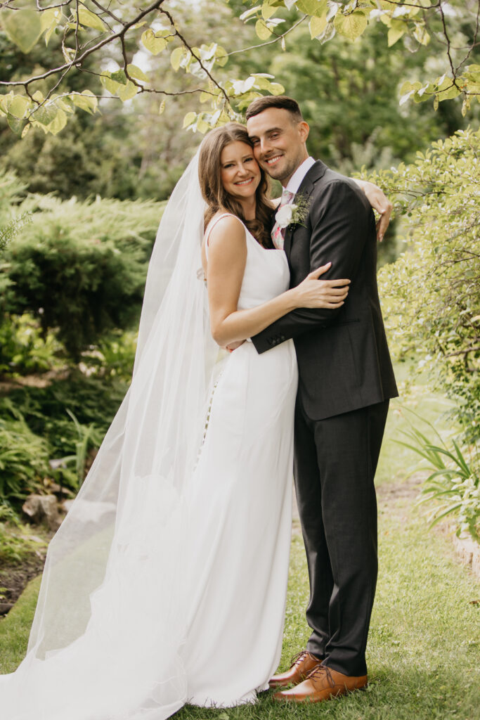 Bride and groom embracing under trees at a summer garden wedding