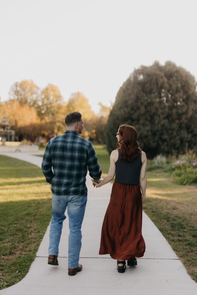 Couple walking hand in hand down a garden path lined with evergreens at golden hour