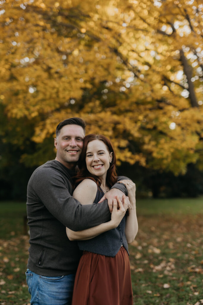 Couple embracing and smiling for the camera under fall trees