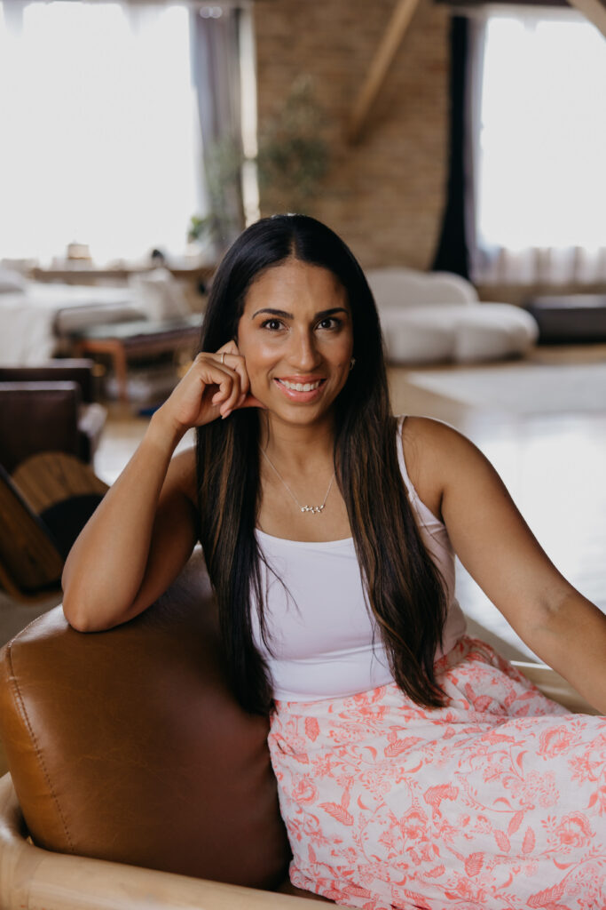Tatiana Budney in a pink floral skirt, hand near her cheek, seated in a loft interior