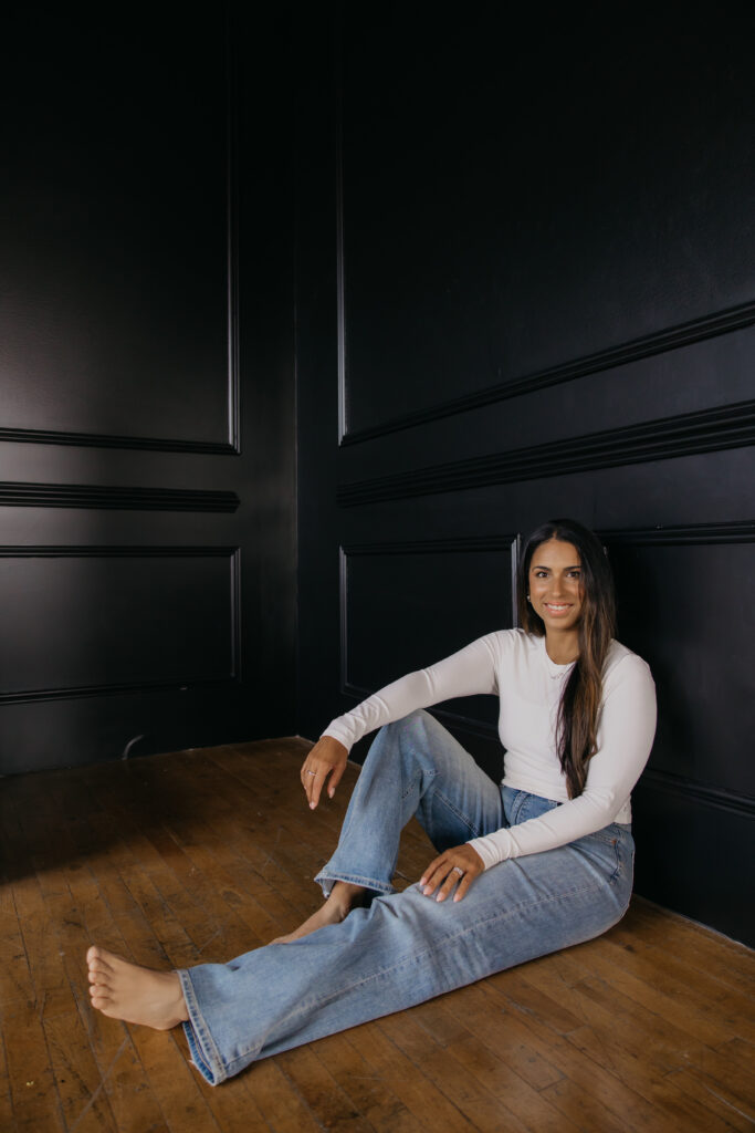 Tatiana Budney in a white button-down and jeans, relaxed and seated on a wood floor