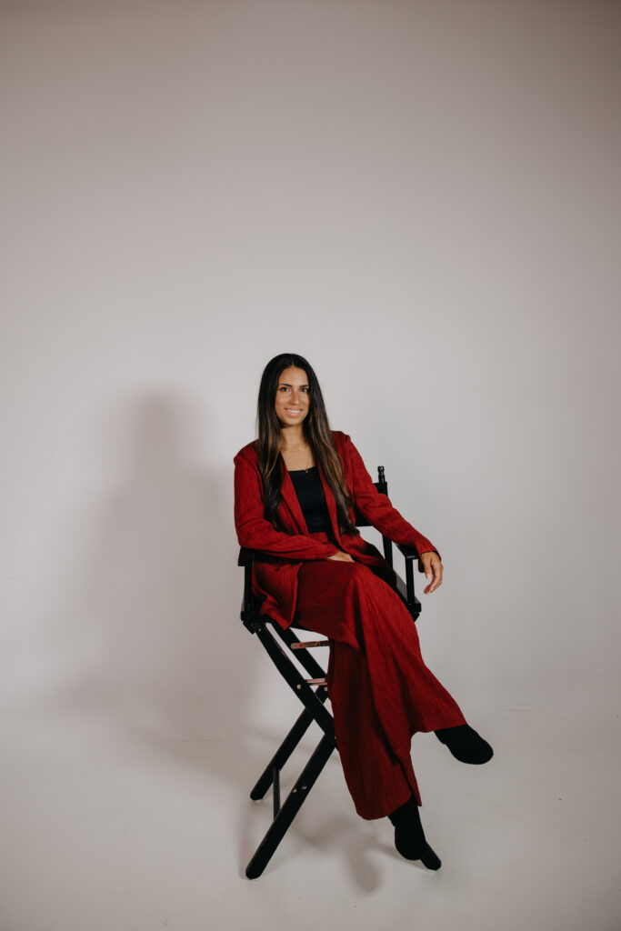 Business headshots in Minneapolis: Tatiana Budney seated in a red duster suit on a black director's chair