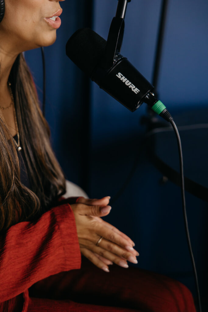 Tatiana Budney in a red duster sleeve, speaking into a Shure microphone in a podcast studio