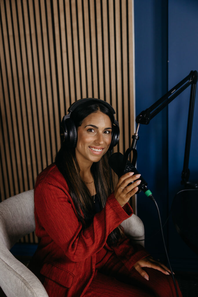 Tatiana Budney in a red duster suit speaking into a microphone, headphones on, in a podcast studio