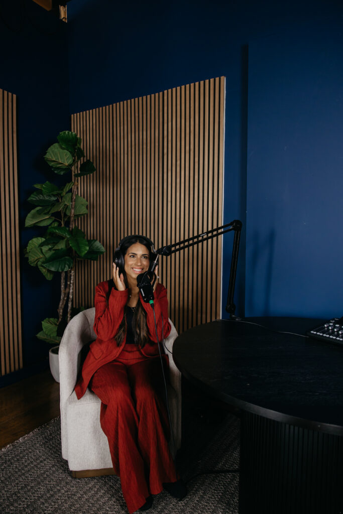 Tatiana Budney in a red duster suit, profile view, speaking into a microphone in a podcast studio