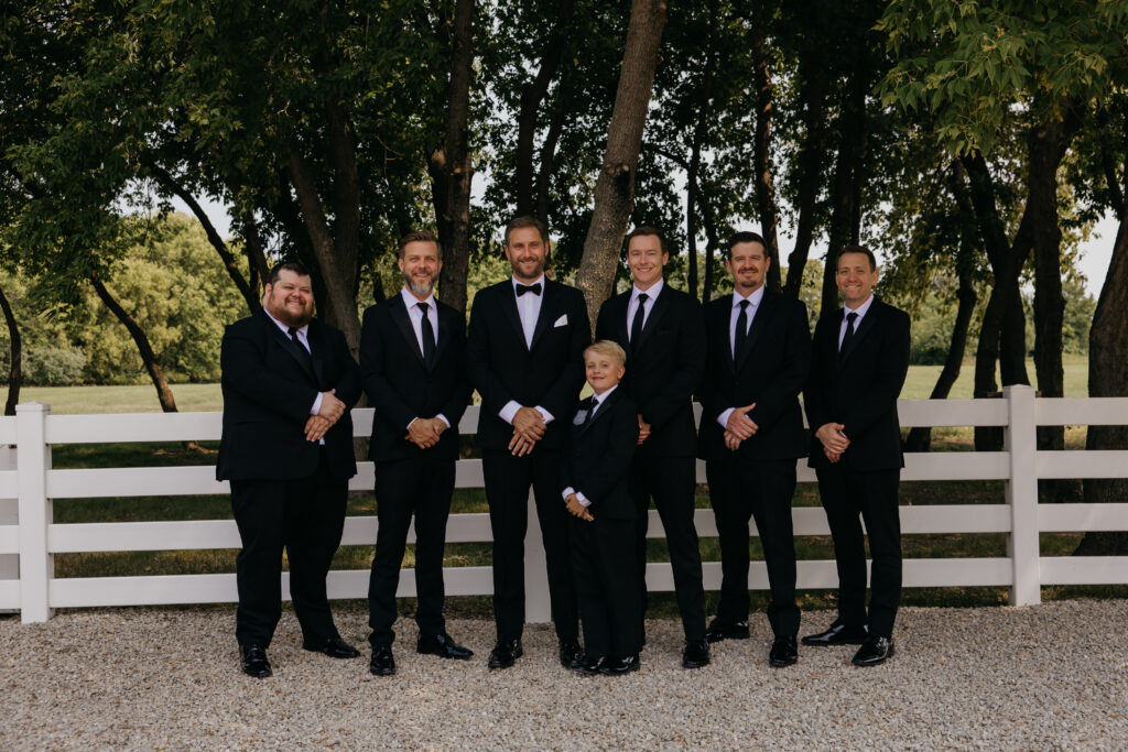 Groomsmen in black suits standing in front of a white fence