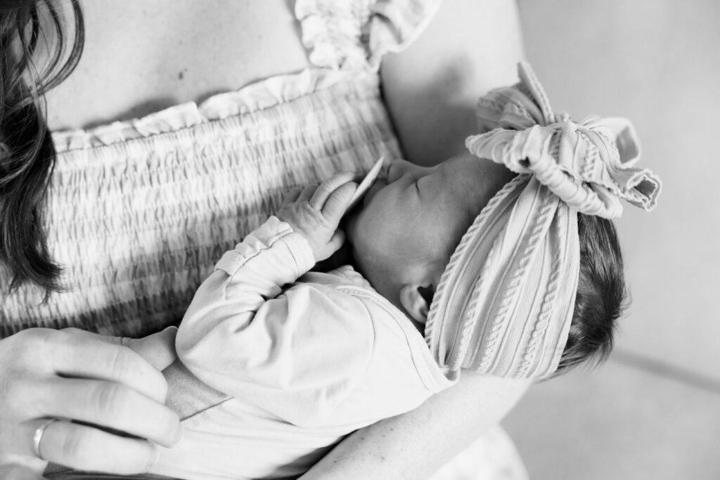 Black and white close-up of mom holding her newborn in a knit bow headband, baby's hand resting on her shirt
