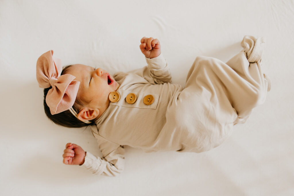Newborn baby lying on a blanket wearing a pink bow headband with arms raised