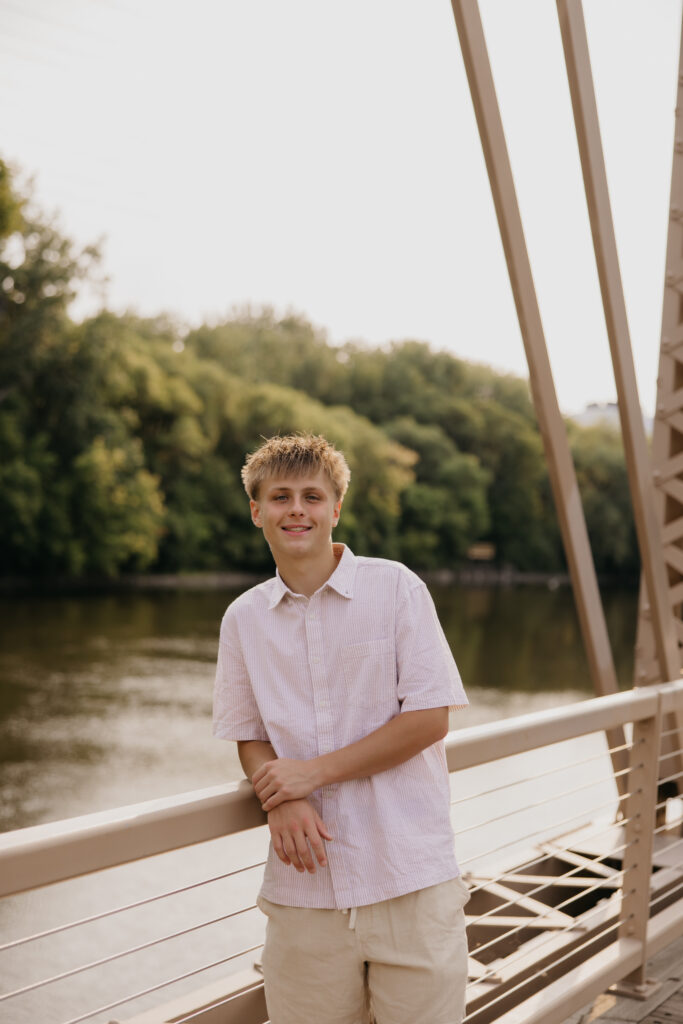 Senior guy in a white polo leaning against a railing on a pedestrian bridge over the river