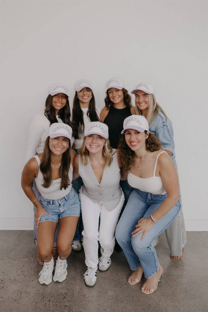 The Wellthy Circle team in matching white caps posed together in a playful group portrait